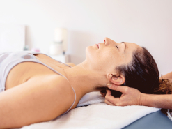 Frau liegt in Rückenlage, die Hände einer therapierenden Person befinden sich unterhalb des Kopfe